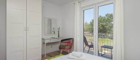 A bedroom with a bed, a desk, a chair, and a balcony with a table and chair.