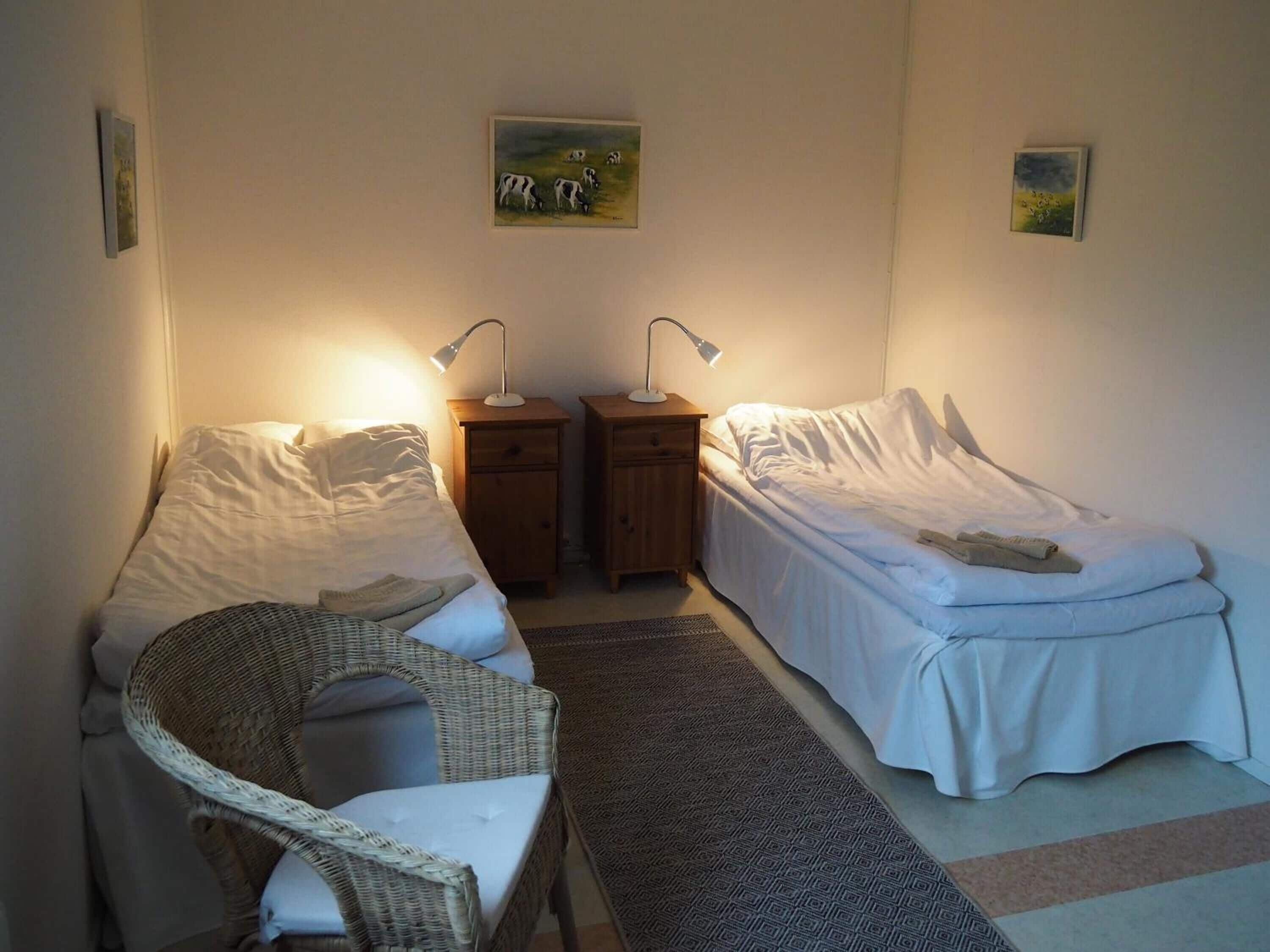 Een knus slaapkamer met twee eenpersoonsbedden, een rieten stoel en twee nachtkastjes met lampen.