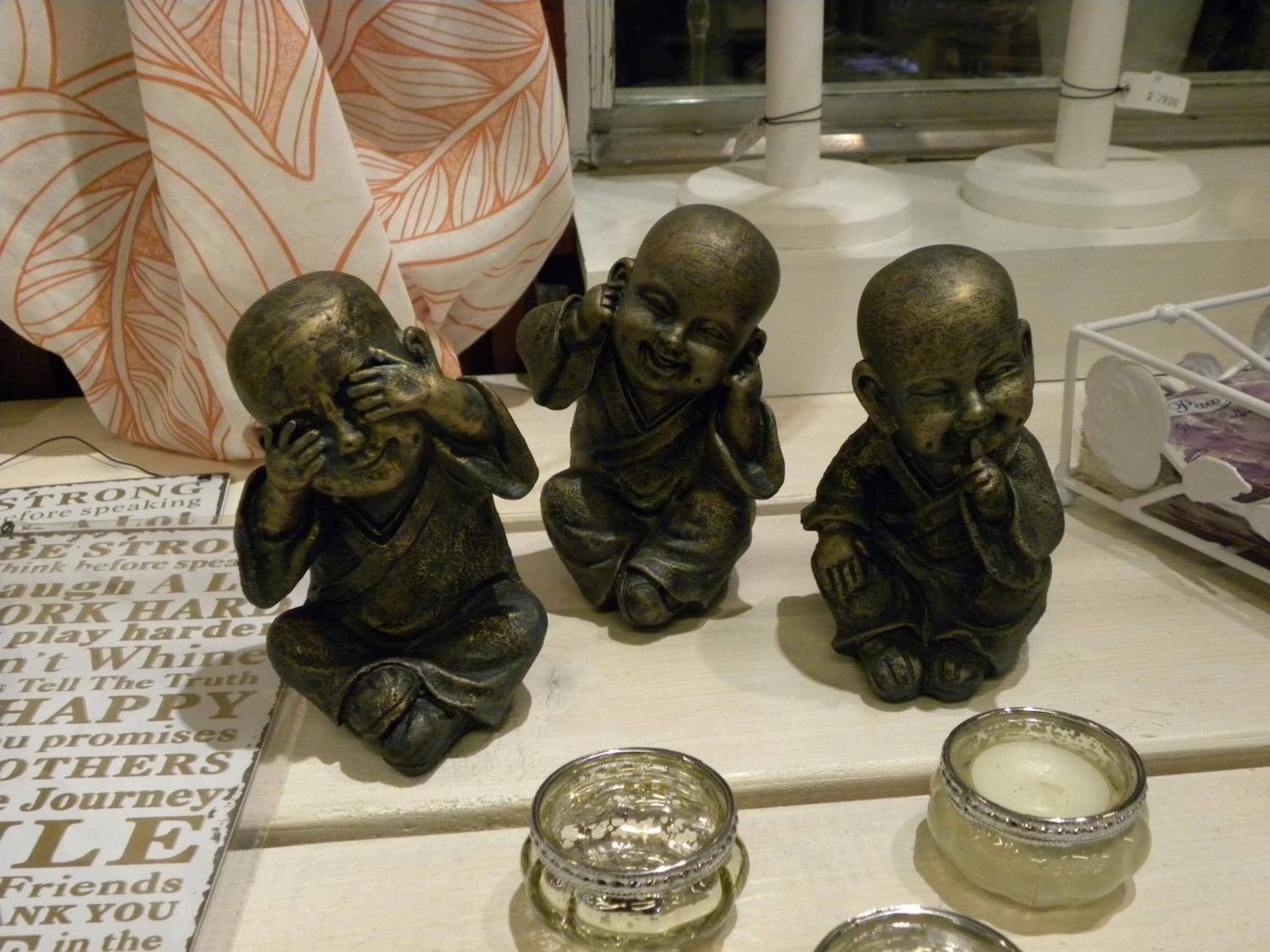 Trois statues de Bouddha en bronze sont posées sur une étagère, avec des bougies et un objet décoratif en arrière-plan.