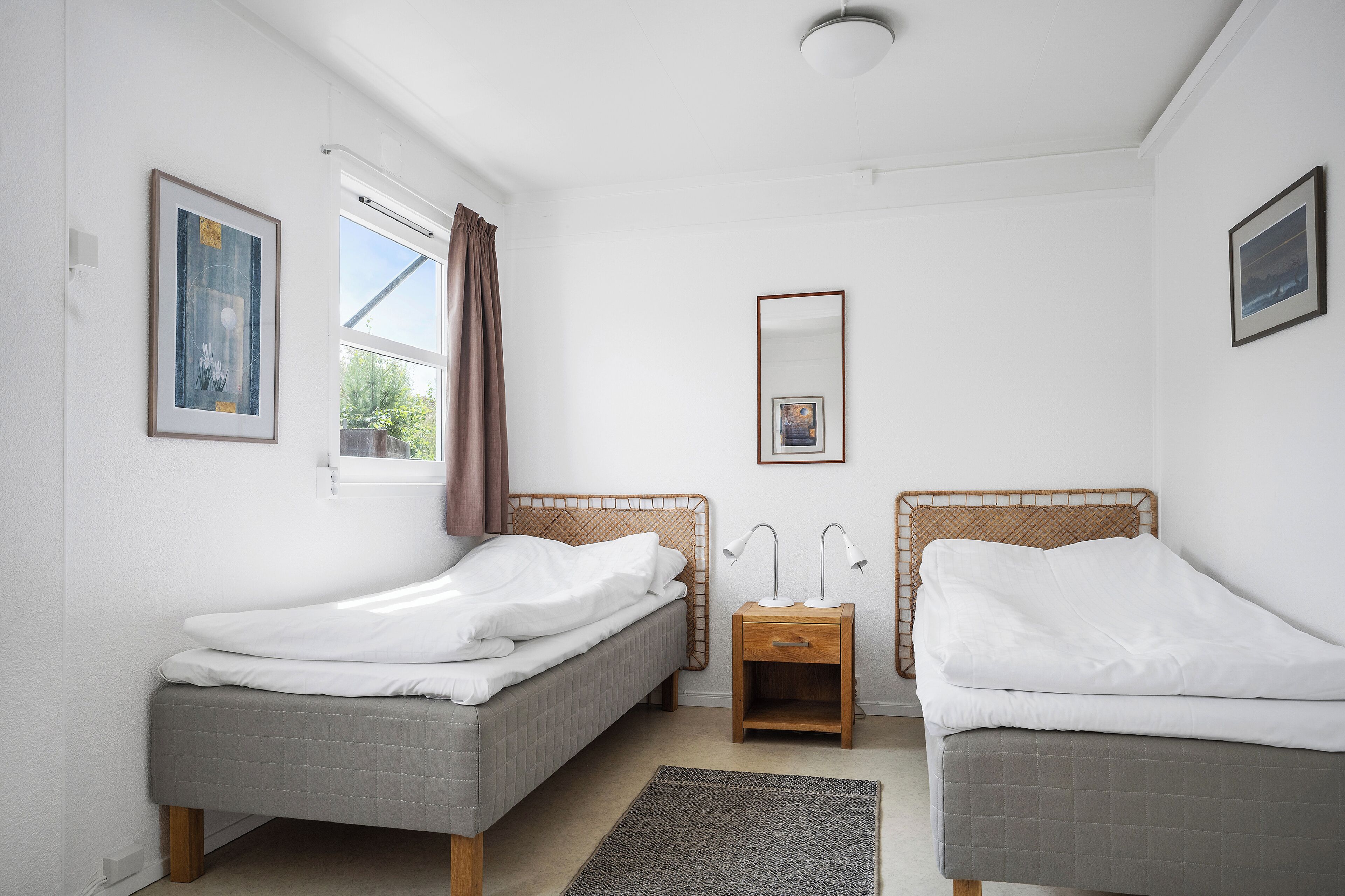 Une chambre avec deux lits, une table de chevet avec des lampes, un miroir et des œuvres d’art encadrées accrochées aux murs.