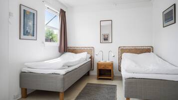 Une chambre avec deux lits, une table de chevet avec des lampes, un miroir et des œuvres d’art encadrées accrochées aux murs.