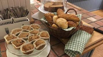 Une table de buffet avec des muffins, du pain et un panier de petits pains.