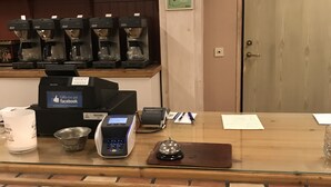 Zona de recepción de hotel con una máquina de café, una caja registradora, un timbre y un letrero que indica la salida.
