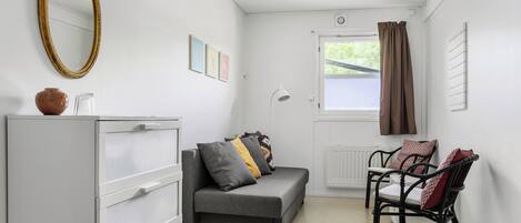 A room with a grey sofa, a white cabinet, a black chair, a mirror, and a window with curtains.