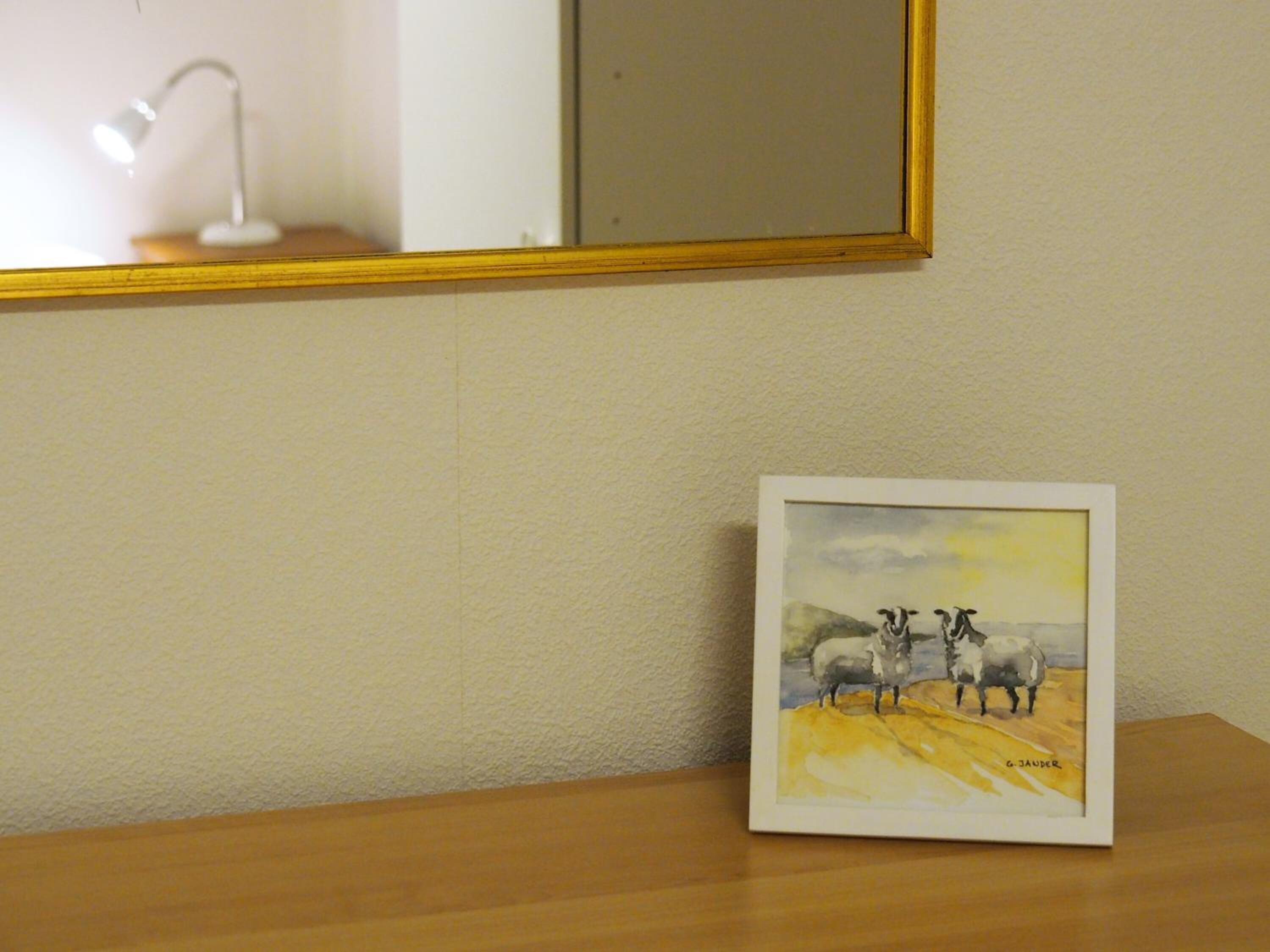 A framed artwork of sheep on a wooden table against a textured wall.