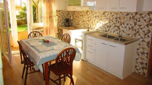 A compact kitchen with white cabinets, a small countertop, and a dining area with a table and chairs. - Apartments Jakša (Pula)