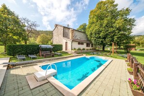 Ein rechteckiger Pool mit gefliestem Sonnendeck, umgeben von einem Holenzaun und Blumentöpfen.