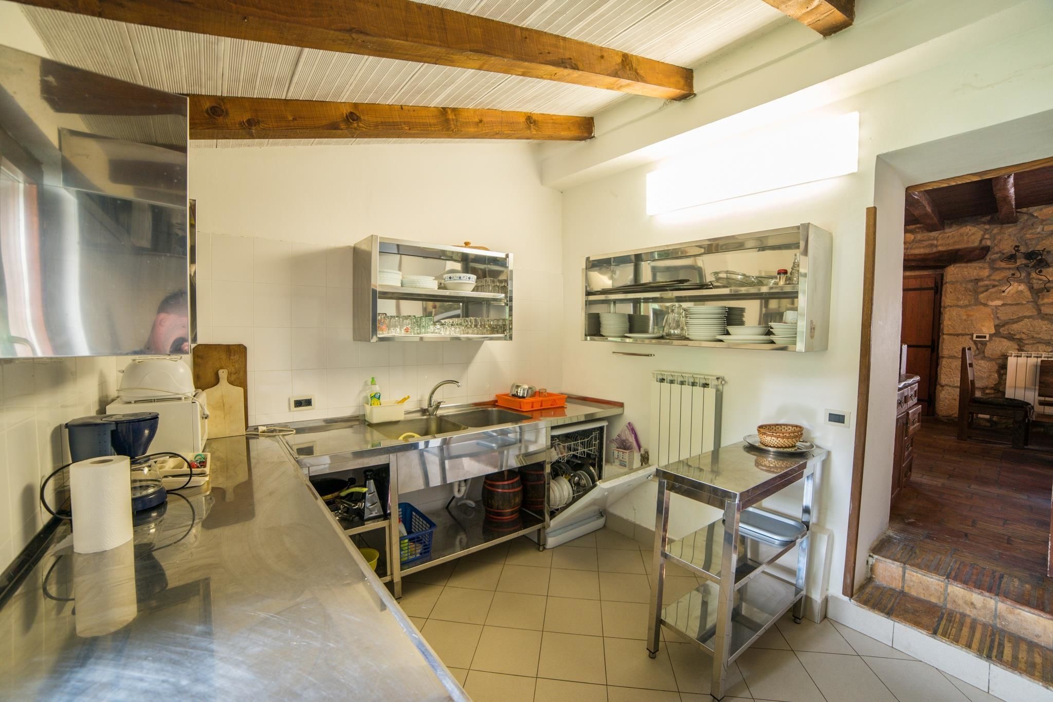 A compact kitchen with stainless steel appliances, wooden beams, and a stone wall.