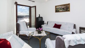 Una habitación con un sofá, sillas, una mesita con flores, un televisor y un cuadro en la pared.