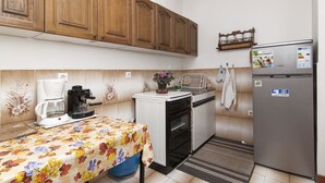 Una pequeña cocina con armarios de madera, una cafetera, un refrigerador y una mesa con mantel floral.