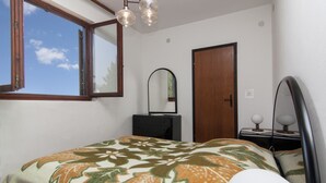 Un dormitorio con cama, cómoda, espejo, puerta y ventana con vista al cielo.