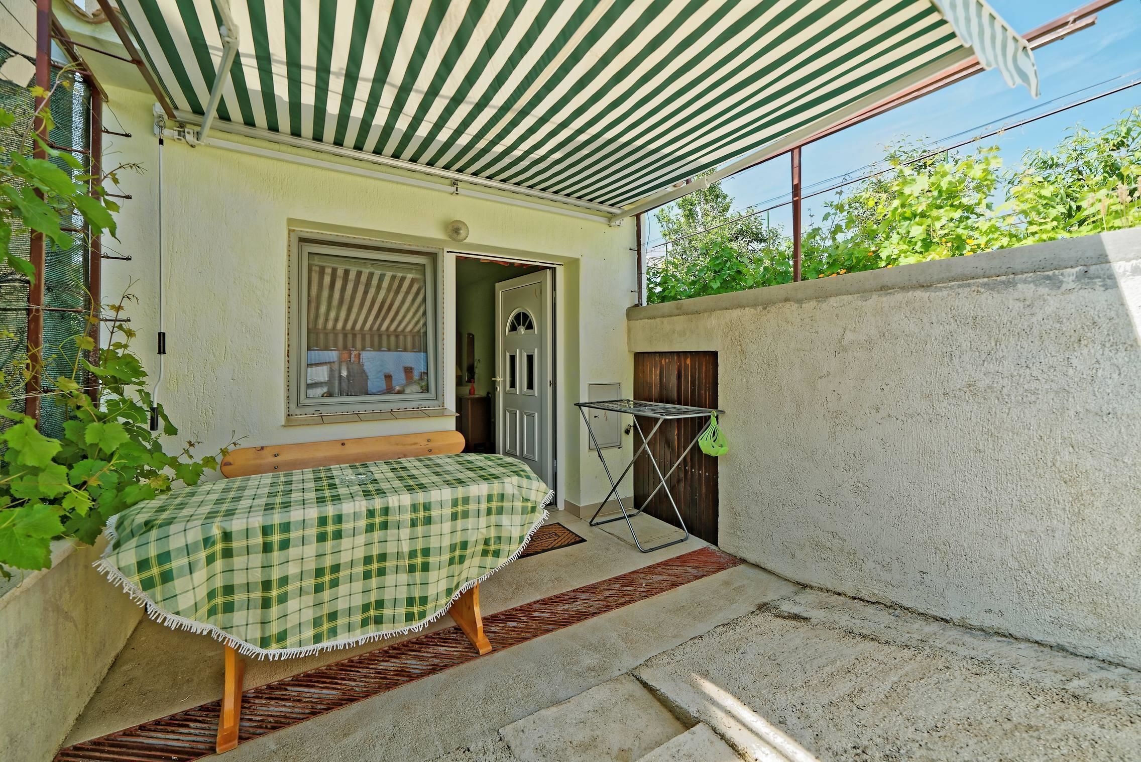 A small, enclosed outdoor area with a checkered table, a bench, and a door leading inside.