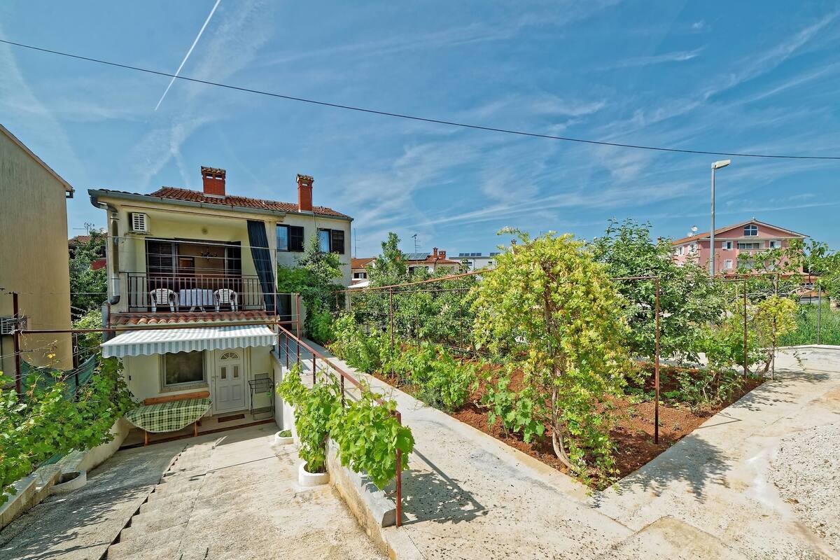 Un immeuble d’habitation doté d’un balcon, d’un jardin avec des vignes et surplombant un ciel bleu dégagé.