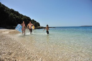 A pebbled beach with clear water and a rocky shoreline.
