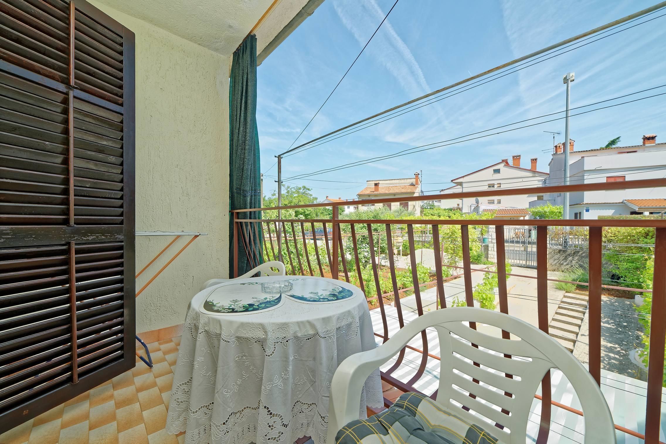 En balkon med et bord og stole, udsigt til gaden og en bygning i baggrunden.