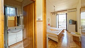 A bedroom with a wooden floor, a bed with a patterned bedspread, a bedside table, a television, and a balcony with a view. - App and Rooms Marojevic (Rovinj)