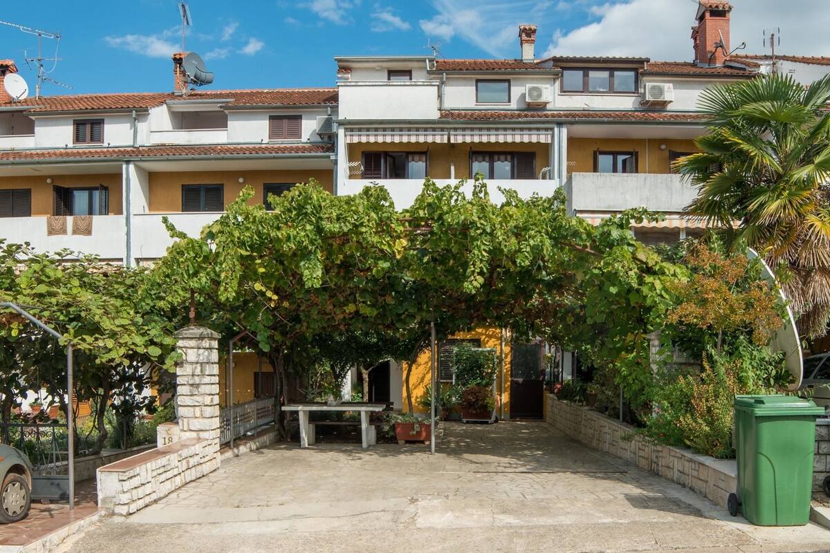Un edificio residencial con un patio cubierto, pilares de piedra y un bote de basura verde.