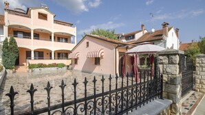 A courtyard with a stone fence, a small building with a red awning, and a multi-story building with balconies. - Apartments Folo (Rovinj)