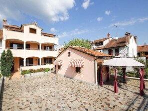A courtyard with a tiled floor, a building with a balcony, and a small structure with a roof. - Apartments Folo (Rovinj)
