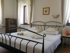 A neatly made bed with white linens and towels, a wooden cabinet, a small table with a lamp, and a picture on the wall.
