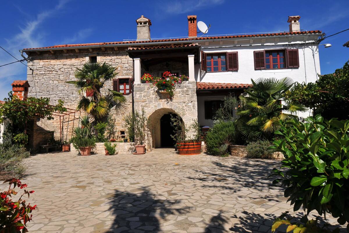 A traditional stone building with a tiled roof, a central archway, and potted plants around the entrance.