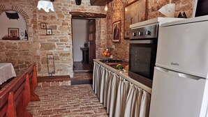 A kitchen with a stone wall, a wooden bench, a white refrigerator, and a hanging light fixture.
