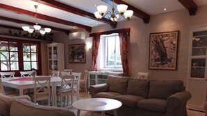 A living room with a brown sofa, white chairs, a round coffee table, and a dining area with a white table and chairs.