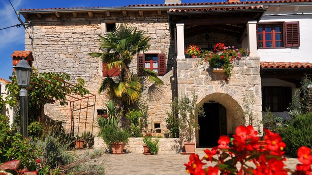 A stone building with a tiled roof, an arched entrance, and potted plants.