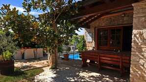 A stone building with a pool, outdoor seating, and a pergola with a tree.
