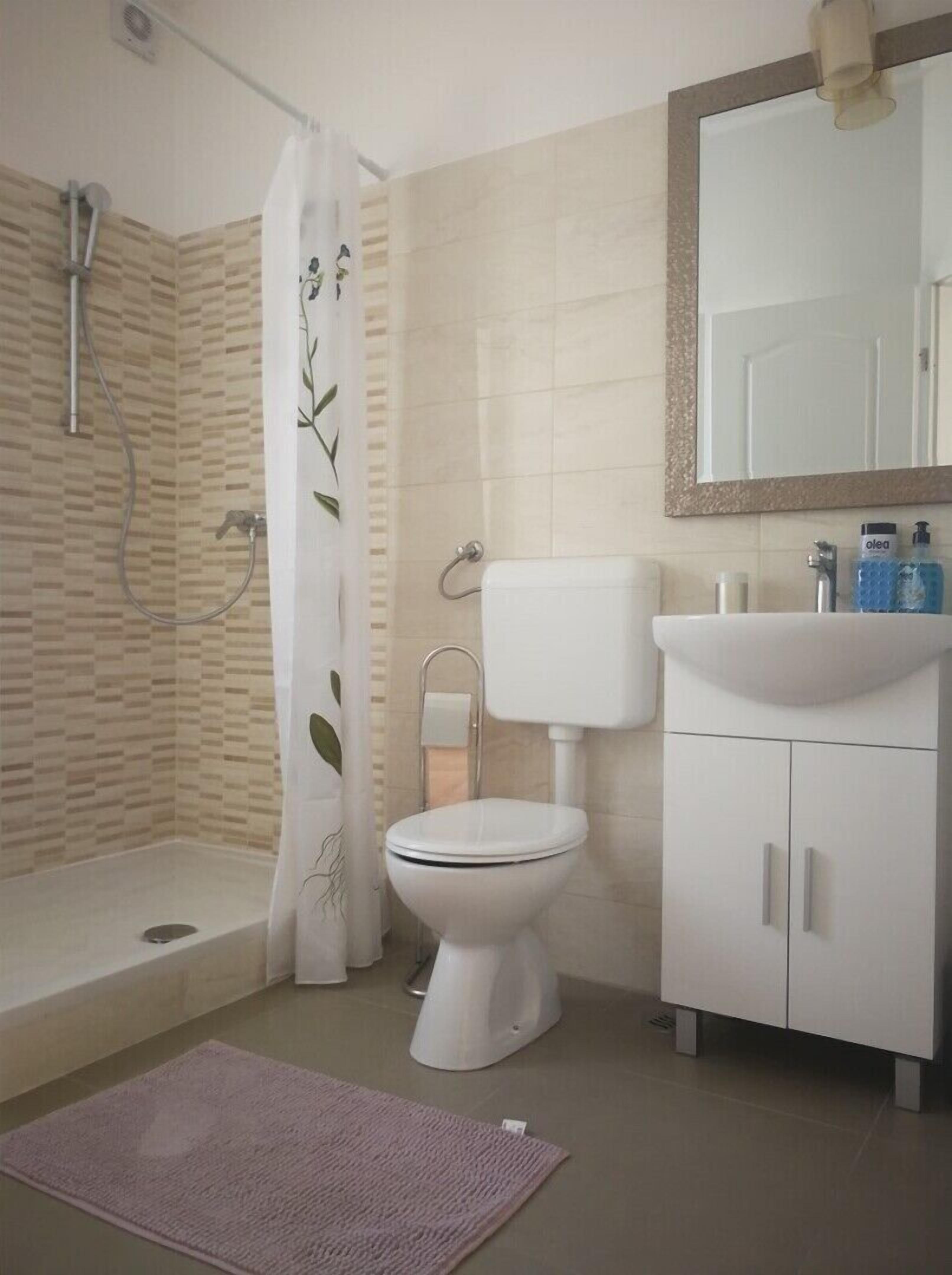 Une salle de bain équipée d’une douche, de toilettes, d’un lavabo et d’un miroir.