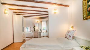 A bedroom with a large bed, wooden beams on the ceiling, a dresser, and a vanity with a mirror.