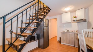 A modern kitchen with wooden flooring, a stainless steel refrigerator, white cabinets, and a wooden staircase with black railings.