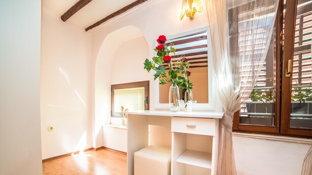 A room with a white desk, a vase with red flowers, and a window with blinds.