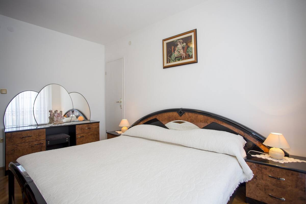 A bedroom with a bed, a dresser, a mirror, a nightstand, and a framed picture on the wall.