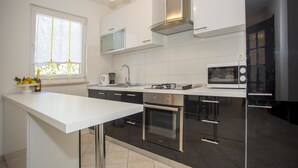 A modern kitchen with white cabinetry, stainless steel appliances, and a window providing natural light. - Apartments Milan Rovinj (Rovinj)