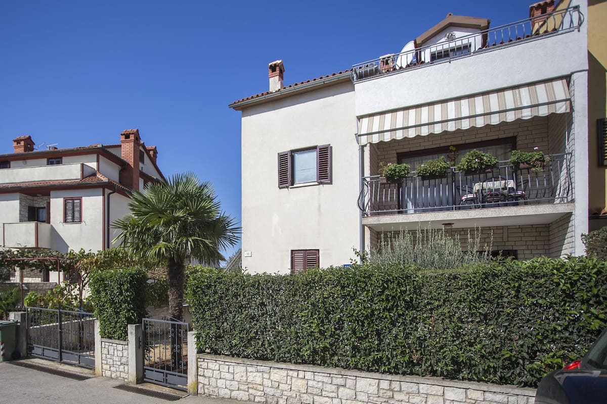 A two-story building with a balcony, a stone wall, and a metal gate.