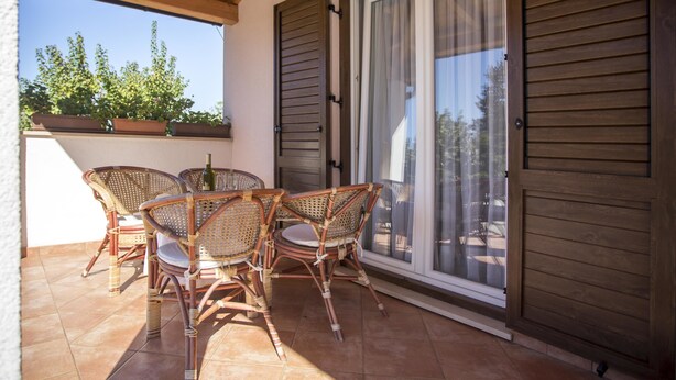 A covered patio with wicker furniture, a table, and a bottle. - Apartments Milan Rovinj (Rovinj)