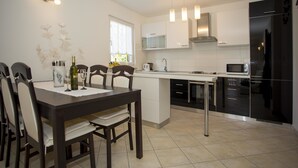 A modern kitchen with white cabinetry, a central island, and a dining area with a dark wooden table and chairs. - Apartments Milan Rovinj (Rovinj)