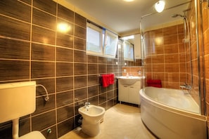 A modern bathroom with dark wood tiles, a bidet, a sink, and a bathtub. - Apartments Orange Medulin (Medulin)