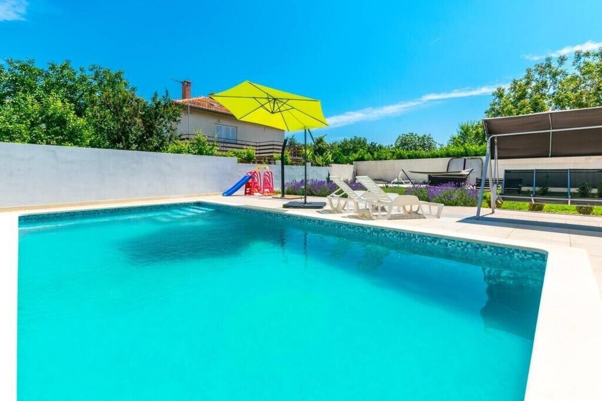 A swimming pool with a yellow umbrella, lounge chairs, and a slide.