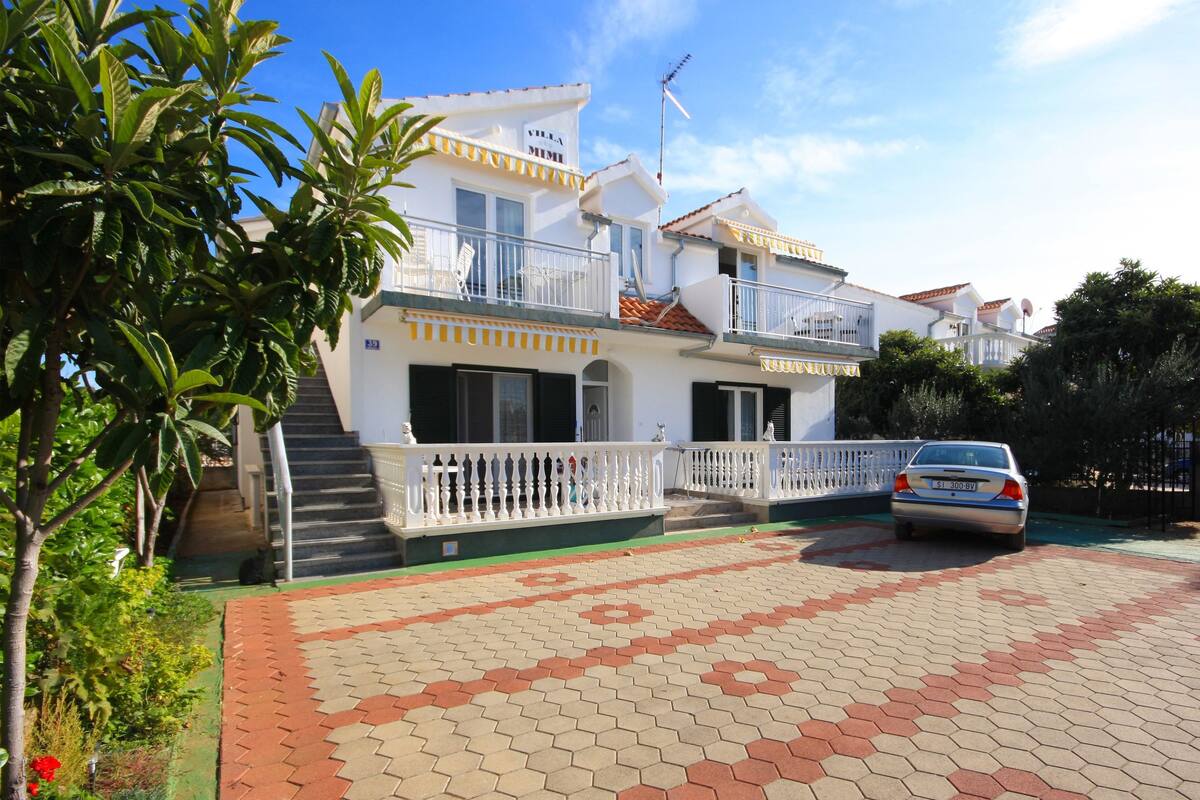 Eine zweistöckige Villa mit Balkon, ein Auto auf der Auffahrt und ein gepflegter Garten.