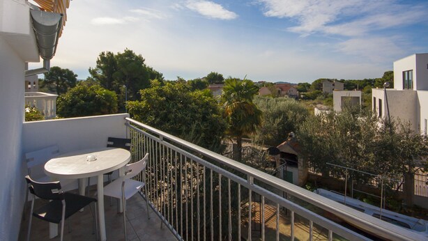 A balcony with a table and chairs, overlooking a residential area with houses and greenery. - Apartment Vinko (Sibenik)