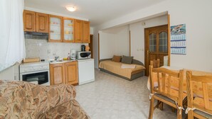 A compact kitchen with wooden cabinets, a microwave, and a small refrigerator. There is a bed with a wooden headboard and a dining table with chairs. - Apartments Silvano 407 (Porec)