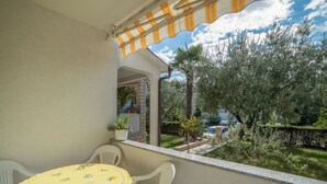 A balcony with a yellow table and chairs, a view of a garden with trees and a car in the background. - Apartments Silvano 407 (Porec)