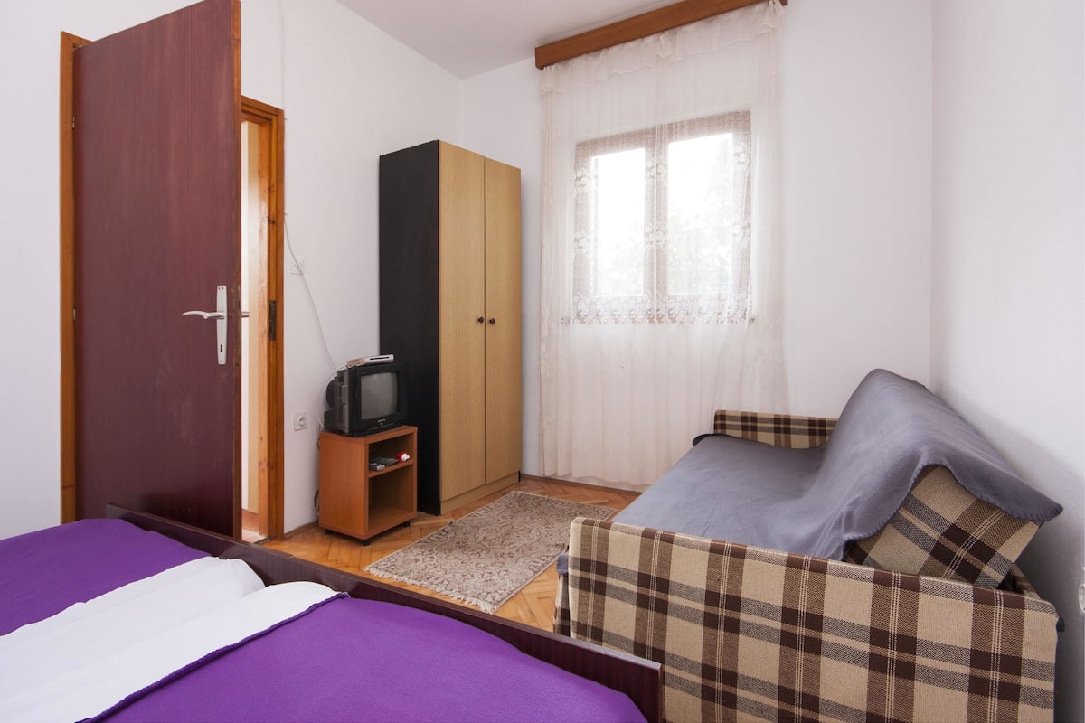 A bedroom with a bed, a wardrobe, a television, and a window with curtains.