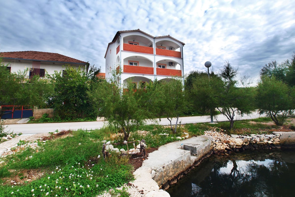 A multi-story building with balconies, a paved pathway, and a small water feature.