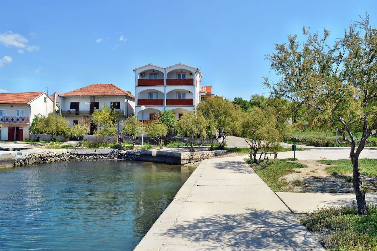 A waterfront property with a canal, a paved walkway, and a multi-story building with balconies.