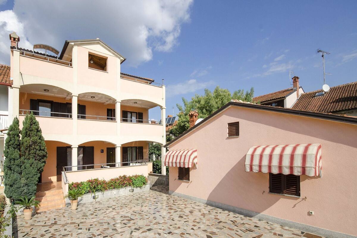 A building with a tiled courtyard, a balcony, and a small garden area with potted plants.