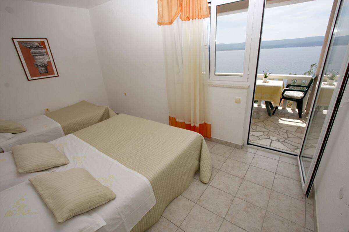 A bedroom with two beds, a balcony with a table and chairs, and a view of the sea.