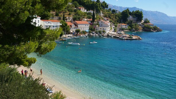 A coastal town with clear waters, a beach, and buildings on a hillside. - Apartments Vesna Mimice (Omis)
